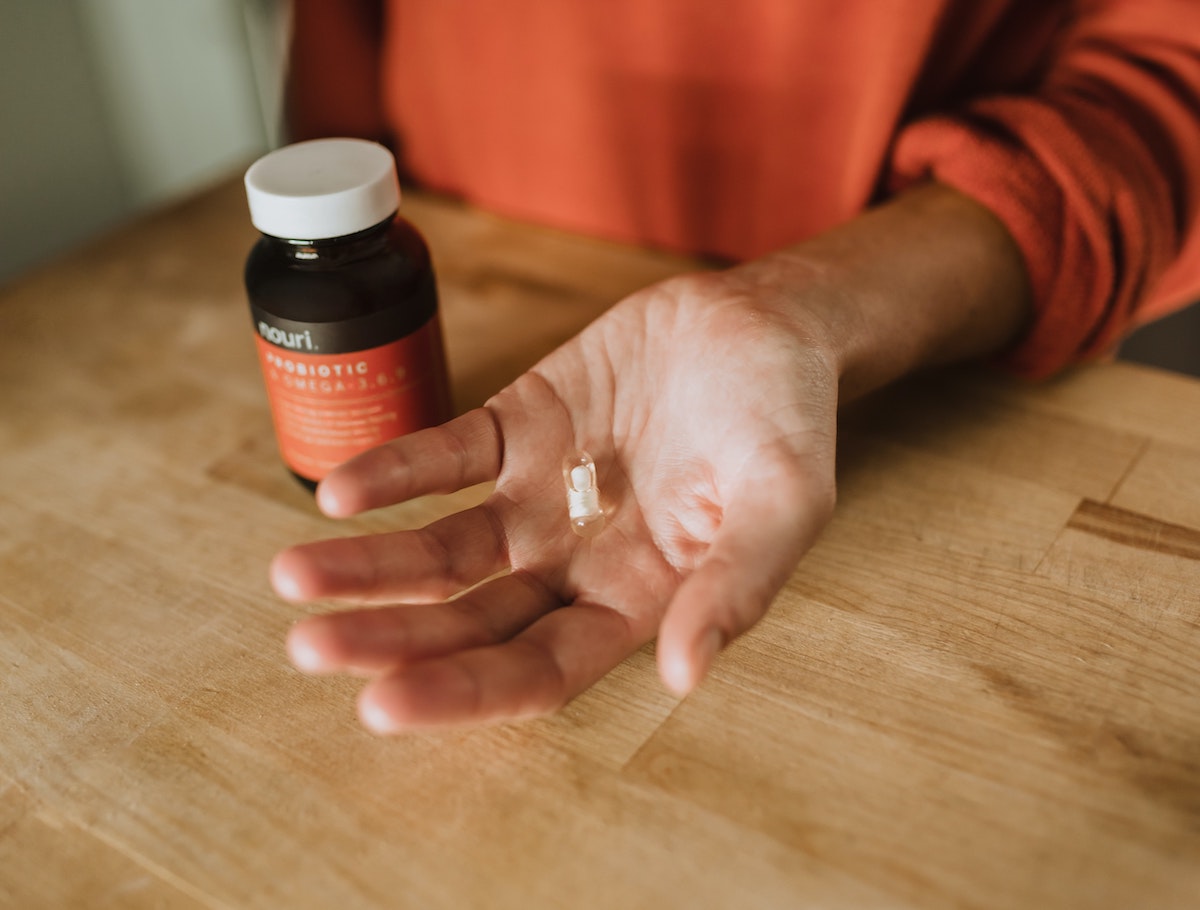 A picture of a woman's hand holding one probiotic tablet, in the background is the probiotic pill bottle.