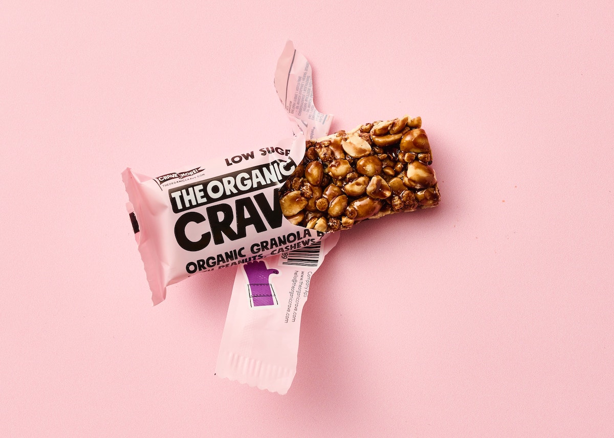 On a pink background is one protein bar. It is in pink wrapping and has been half opened.