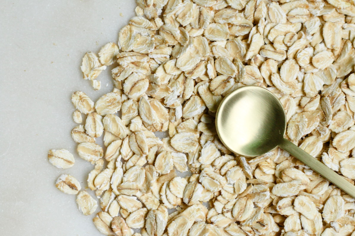 A picture of oats spread across the picture and in the middle is a gold spoon.