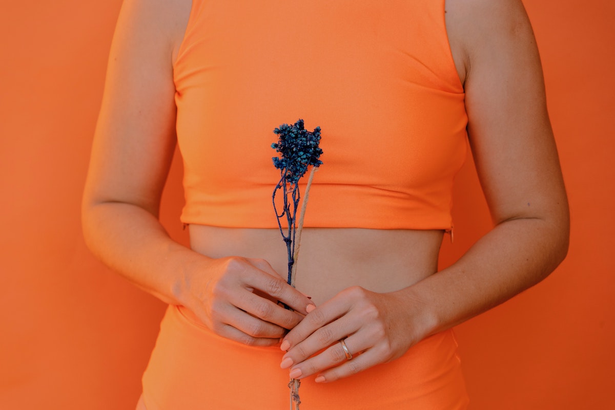 A woman dressed in an orange crop top and leggings, holding a flower over her stomach