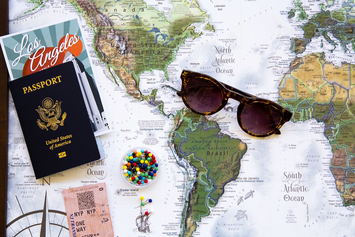 The background is a world map and on top there is a passport with some postcards inside it and next to that is a pair of sunglasses.